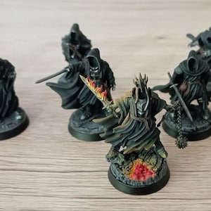 Puede incluir: Un grupo de siete figuras en miniatura pintadas de negro, incluyendo una figura con una corona y una espada llameante, de pie sobre bases redondas. Las figuras llevan túnicas negras y sostienen espadas.