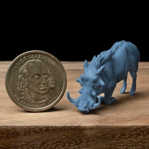 Könnte beinhalten: Eine blaue Plastikfigur eines Warzenschweins mit einem eingerollten Schwanz und großen Hauern. Die Figur steht neben einer US-amerikanischen Ein-Dollar-Münze mit dem Bild von James Madison, dem vierten Präsidenten der Vereinigten Staaten. Die Münze trägt die Aufschrift "James Madison 4th President 1809-1817".