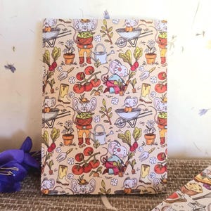 Peut inclure: Une couverture de carnet de couleur crème avec un motif répétitif de souris faisant du jardinage. Les souris portent des salopettes et des chapeaux et tiennent des outils de jardinage. Le motif comprend également des tomates, des carottes et d'autres éléments de jardin.