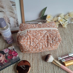 Può includere: Un beauty case trapuntato color pesca con un motivo floreale bianco, un pennello per il trucco, rossetti e una palette di ombretti. Sono presenti anche un flacone di spray per il corpo e uno specchietto compatto.