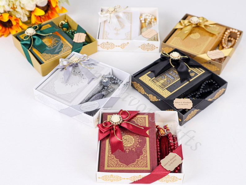 K&ouml;nnte beinhalten: F&uuml;nf Geschenkboxen mit goldenen Verzierungen und dekorativen Schleifen enthalten einen Koran und Gebetsperlen. Die Boxen sind in verschiedenen Farben, darunter Gr&uuml;n, Wei&szlig;, Gold, Schwarz und Rot.