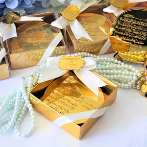 May include: Gold gift boxes with white ribbon and a small gold mirror with Arabic calligraphy. The boxes contain a white pearl prayer beads with a gold tassel.