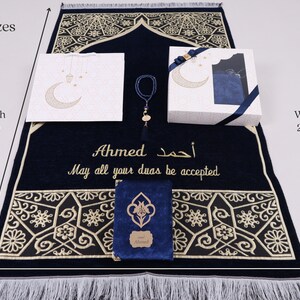 May include: A blue prayer rug with gold embroidery and a personalized inscription that reads "Ahmed أحمد May all your duas be accepted". The rug is 51 inches long and 27 inches wide. The set includes a matching prayer book, a prayer bead necklace, and a gift bag.