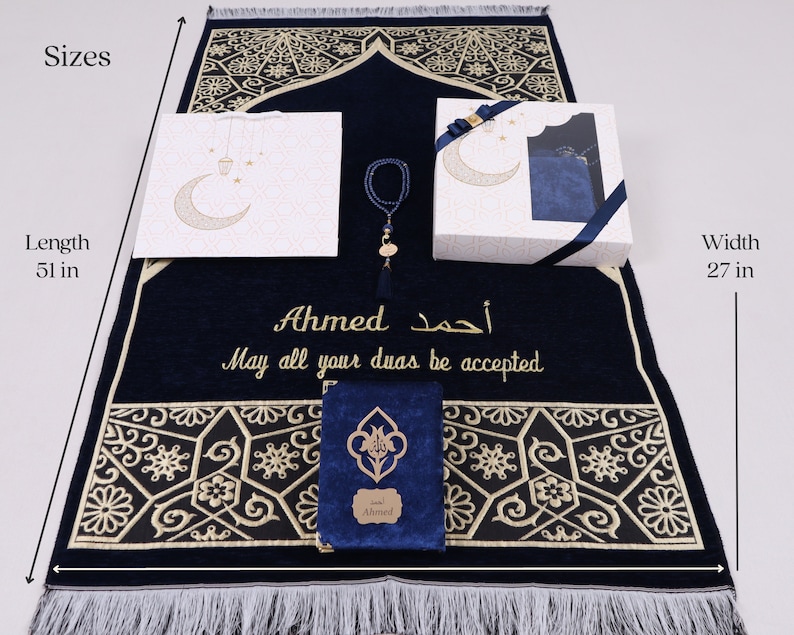 May include: A blue prayer rug with gold embroidery and a personalized inscription that reads "Ahmed أحمد May all your duas be accepted". The rug is 51 inches long and 27 inches wide. The set includes a matching prayer book, a prayer bead necklace, and a gift bag.