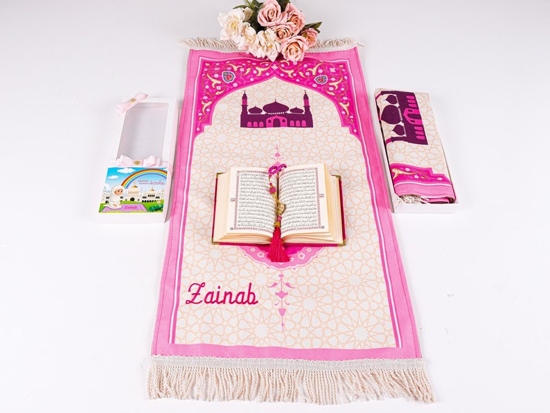 Peut inclure: Un tapis de pri&egrave;re rose avec un motif de mosqu&eacute;e, un Coran et une &eacute;charpe assortie. Le tapis est personnalis&eacute; avec le nom "Zainab". Une bo&icirc;te cadeau avec une illustration d'arc-en-ciel et de mosqu&eacute;e est &eacute;galement incluse. L'ensemble est con&ccedil;u pour la pri&egrave;re islamique.