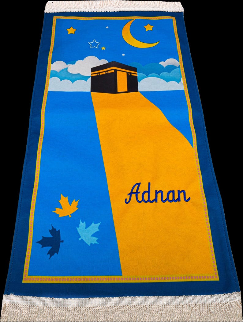 Peut inclure: Tapis de pri&egrave;re bleu avec un chemin jaune menant &agrave; une structure noire. Le tapis pr&eacute;sente un ciel bleu avec une lune, des &eacute;toiles et des nuages. Le nom "Adnan" est &eacute;crit en bleu.