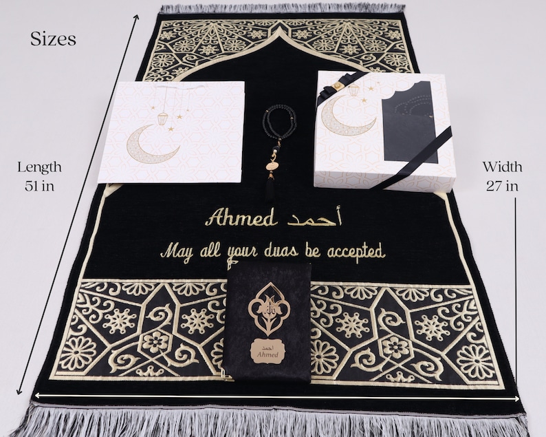 May include: A black prayer rug with gold embroidery and a personalized inscription that reads "Ahmed أحمد May all your duas be accepted". The rug is 51 inches long and 27 inches wide. It comes with a matching prayer mat, a small gift box, and a prayer bead bracelet.