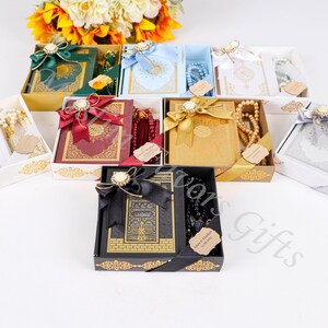 May include: Assortment of gift boxes containing a Quran and prayer beads. The boxes are decorated with gold trim and ribbons. The prayer beads are in various colors, including white, red, and black.