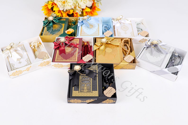 May include: Assortment of gift boxes containing a Quran and prayer beads. The boxes are decorated with gold trim and ribbons. The prayer beads are in various colors, including white, red, and black.