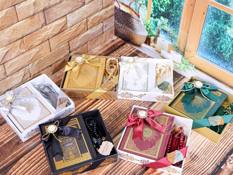 K&ouml;nnte beinhalten: Sechs Geschenkboxen mit einem Koran und Gebetsperlen. Die Boxen sind mit B&auml;ndern und Schleifen verziert. Die Boxen sind in verschiedenen Farben, darunter Gold, Wei&szlig;, Schwarz, Rot und Gr&uuml;n.