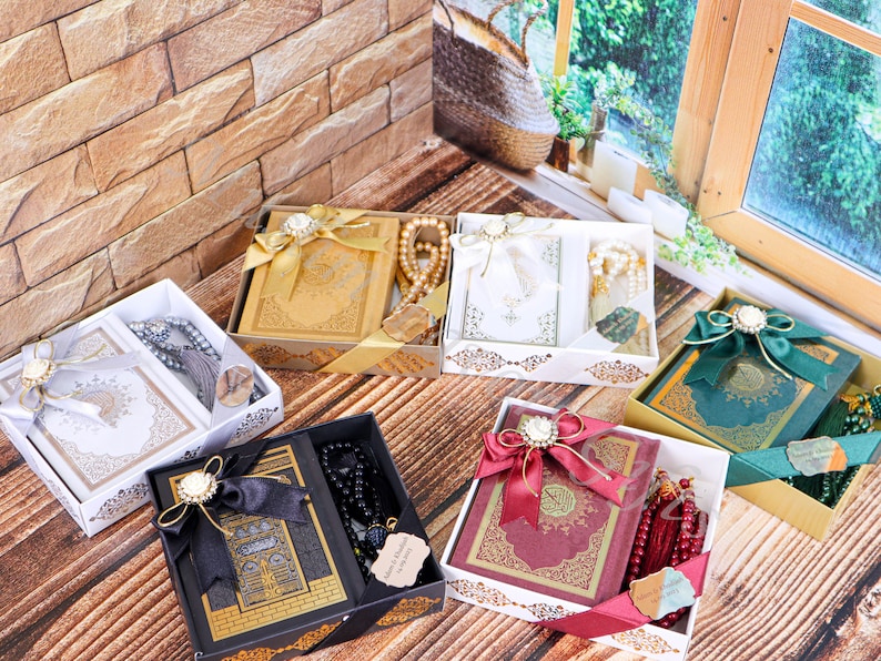 May include: Six gift boxes containing a Quran and prayer beads. The boxes are decorated with ribbons and bows. The boxes are in various colors, including gold, white, black, red, and green.