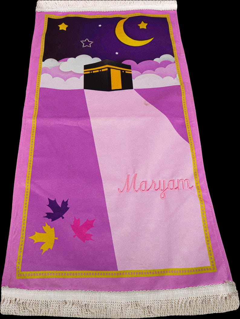 May include: A rectangular prayer rug with a purple and pink design. The top features a night sky with a crescent moon, stars, and clouds above a black building with a gold door. The name "Maryam" is embroidered in pink.