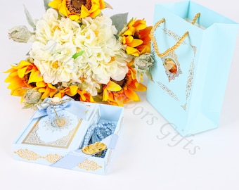 May include: A light blue gift box with gold trim and a decorative design. The box contains a small blue book and a set of blue prayer beads. The box is surrounded by a bouquet of sunflowers and white hydrangeas.