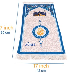 May include: A prayer rug, 37 inches long and 17 inches wide, featuring a mosque design and geometric patterns. The rug has a blue border and fringe, with the name "Amir" printed on it. The central design includes a gold and blue emblem.