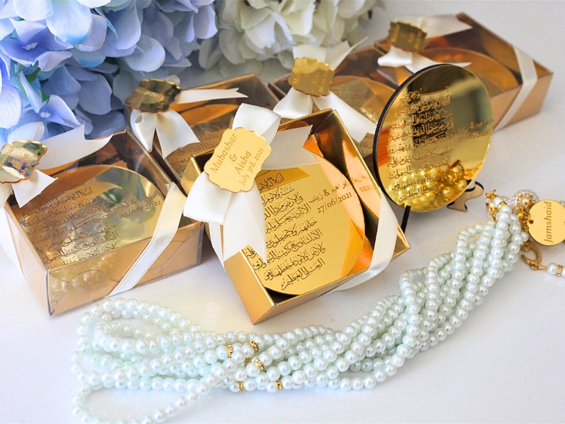 May include: Gold gift boxes with white ribbon and a small gold mirror with Arabic calligraphy. The boxes contain a small gold mirror with Arabic calligraphy. A white pearl prayer beads with a gold charm.