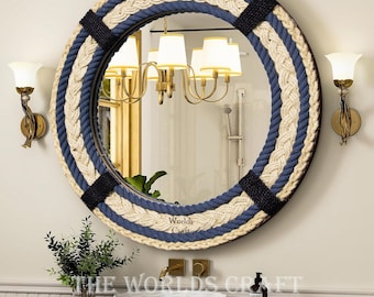 May include: A round mirror with a nautical rope frame in blue and beige. The mirror is hanging on a white wall above a white sink and countertop.