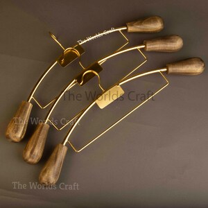 May include: Three clothes hangers featuring gold-toned metal frames and dark brown wooden ends. Each hanger includes a central hook and a rectangular plate with the text The Worlds Craft printed in white. The design combines metallic and wood elements.