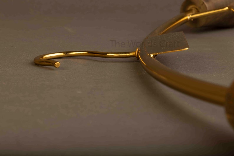 May include: A gold-toned metal clothes hanger featuring a curved hook and a rectangular tag with the text The Worlds Craft printed on it. The hanger has a smooth, polished finish and a curved frame designed for hanging garments in a closet.