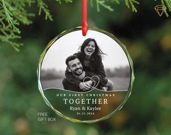 Op de afbeelding: Een transparante glazen kerstbal met een zwart-witfoto van een stel. De kerstbal heeft de tekst "Our First Christmas Together", "Ryan & Kaylee" en de datum "01.21.2024".