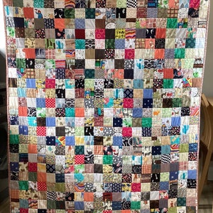 May include: A colourful quilt made of many different fabric squares. The quilt is made up of a variety of patterns and colours, including red, blue, green, yellow, and brown. The quilt is a patchwork of different fabrics, and each square is unique.