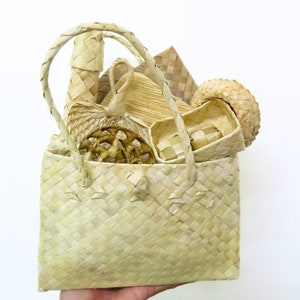 May include: A woven straw tote bag filled with various woven straw items, including a small basket, a fan, and a round decorative piece. The bag is light brown and has a woven pattern.