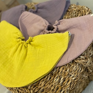 May include: Three muslin baby bibs in a wicker basket. The bibs are in shades of yellow, purple, and light purple.