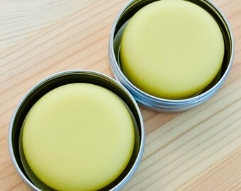 May include: Two round containers with lids, each containing a yellow balm or salve. The containers are made of metal and have a silver finish.