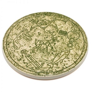 May include: A round ceramic plate with a green and white design. The plate features a deer, a fish, a bird, and other symbols. The plate is a decorative piece with a rustic look.