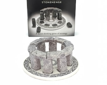 May include: A Stonehenge game set with a circular base and gray stone pieces. The box shows the game's name, "English Heritage Stonehenge", and the phrase "A quick thinking game of strategy".