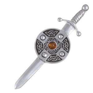 May include: Silver kilt pin featuring a Celtic knot design and an amber stone at its centre. The pin is shaped like a sword with a shield.