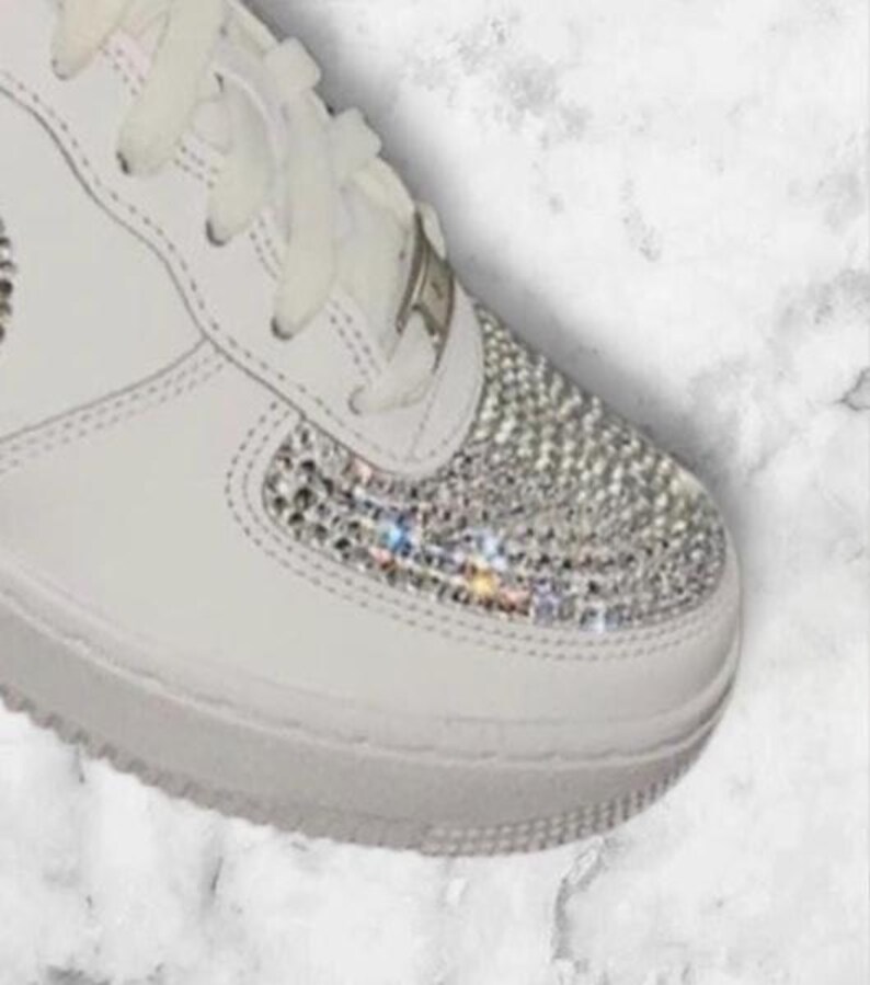 K&ouml;nnte beinhalten: Wei&szlig;e Lederschuhe mit wei&szlig;en Schn&uuml;rsenkeln und einer glitzernden, mit Kristallen besetzten Zehenkappe.