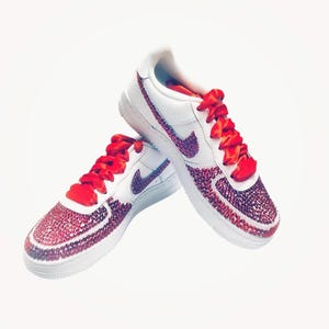 Peut inclure: Des baskets basses blanches avec des lacets en ruban rouge et un design en strass rouge.