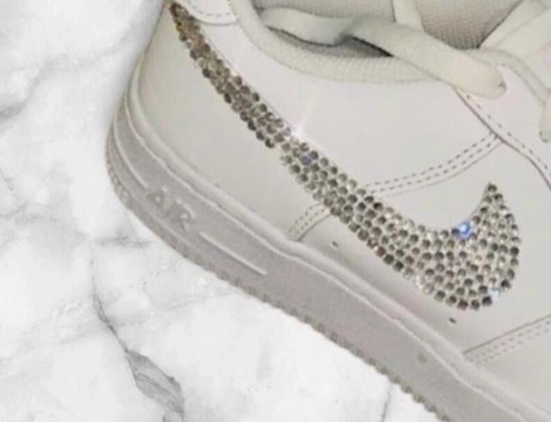 K&ouml;nnte beinhalten: Wei&szlig;e Lederschuhe mit einem mit Diamanten besetzten Nike-Swoosh.