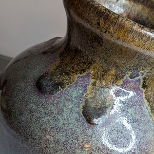May include: A large, round ceramic vase with a mottled glaze in shades of brown, purple, and green. The vase has a wide, rounded opening and a slightly flared lip.
