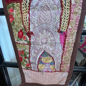 May include: A colorful patchwork tapestry with intricate embroidery and sequins. The tapestry features a variety of fabrics and textures, including velvet, silk, and cotton. The colors are vibrant and rich, and the overall design is very detailed and intricate.