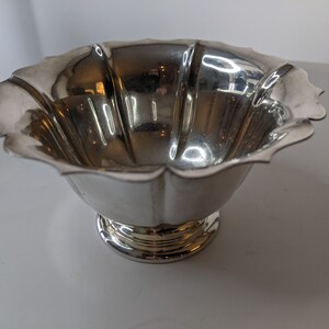 May include: A silver bowl with a scalloped edge and a fluted design. The bowl has a round base.