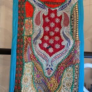 May include: A colorful patchwork wall hanging with intricate embroidery and sequins. The hanging features a variety of colors, including red, blue, green, gold, and silver. The fabric is a mix of textures, including velvet, satin, and lace.