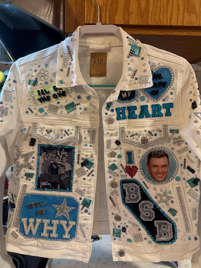 White custom denim jacket with blue and silver rhinestones, patches, and photo details.