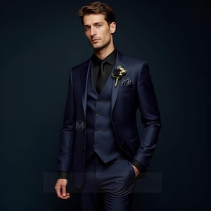 Pode incluir: Um fato azul marinho de três peças com camisa e gravata pretas. O fato apresenta um casaco de dois botões, um colete e calças a condizer. Uma flor preta e um lenço de bolso adicionam um toque de elegância. O fato é feito sob medida e tem um acabamento acetinado.