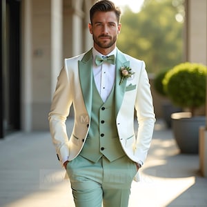 Puede incluir: Un traje de tres piezas en marfil y verde salvia. El traje incluye una chaqueta con solapas verde salvia, un chaleco a juego y pantalones. Una camisa blanca y una pajarita verde salvia completan el conjunto. Un pequeño ojal floral está prendido a la chaqueta.