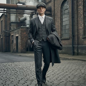 May include: A gray pinstripe suit with a matching vest and flat cap. The suit is worn with a white collared shirt and black shoes. A gray overcoat is draped over the arm. The setting is an industrial brick building.