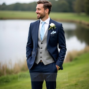 May include: A navy blue suit with a light gray vest, light blue tie, and white shirt. A white flower and light blue pocket square add detail. The suit is worn outdoors with a green background.