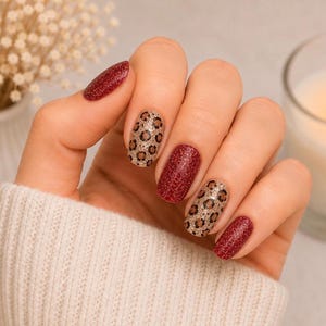 Peut inclure: Ongles arborant une manucure décorative aux motifs alternés. Trois ongles sont recouverts d'un vernis rouge profond à paillettes, tandis que deux ongles présentent une base beige avec un motif léopard noir et marron et une finition pailletée.