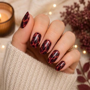 May include: Oval-shaped fingernails featuring a glossy finish with a dark red and black leopard print pattern. The nails are groomed to a smooth, rounded edge, showcasing a consistent animal-inspired design across all five visible fingernails.