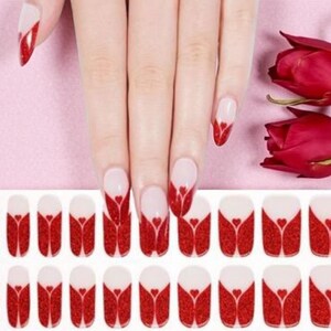 May include: A sheet of nail wraps featuring a French manicure design with a white base and a red glitter heart-shaped tip. The nail stickers are arranged in two rows on a rectangular backing, showcasing a consistent pattern of red glitter.