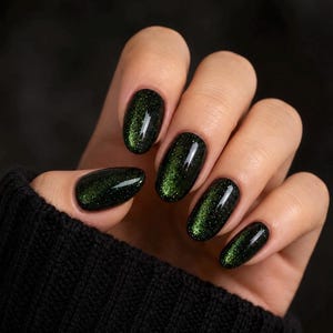 May include: Oval-shaped fingernails featuring a dark black base color with a shimmering, magnetic forest green cat-eye effect. The polish has a high-gloss finish that reflects light, creating a deep, multidimensional appearance across each nail.