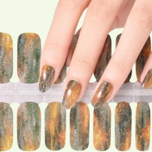 Peut inclure: Un ensemble de bandes de vernis à ongles présentant un motif marbré avec des nuances mélangées de vert foncé, de gris anthracite et d'or métallique. Les bandes adhésives rectangulaires sont disposées sur deux rangées sur un support gris clair.