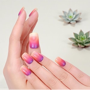 May include: A hand displaying ombre-style artificial nails with a gradient of colors from light peach to vibrant pink and purple. Two small succulent plants are in the background. The nails are square-shaped and have a glossy finish.