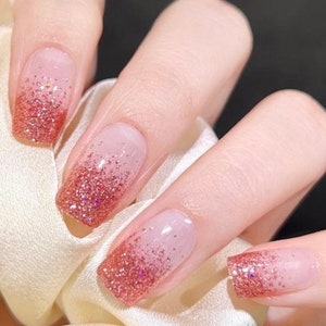May include: Close-up of a hand with five nails painted with a gradient of pink and glitter.