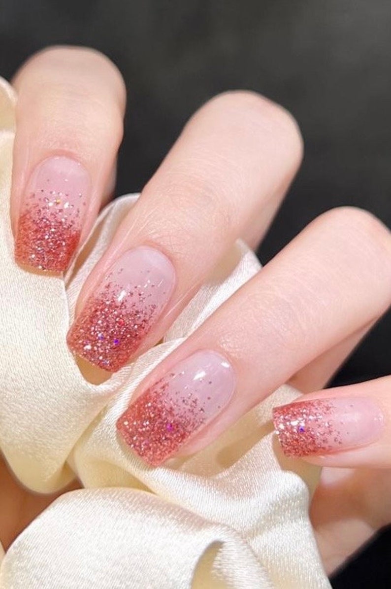 May include: Close-up of a hand with five nails painted with a gradient of pink and glitter.